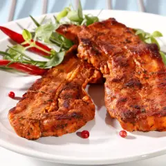 Dwa soczyste plastry boczku na grilla, przyprawione i udekorowane papryczkami chili i zieleniną.