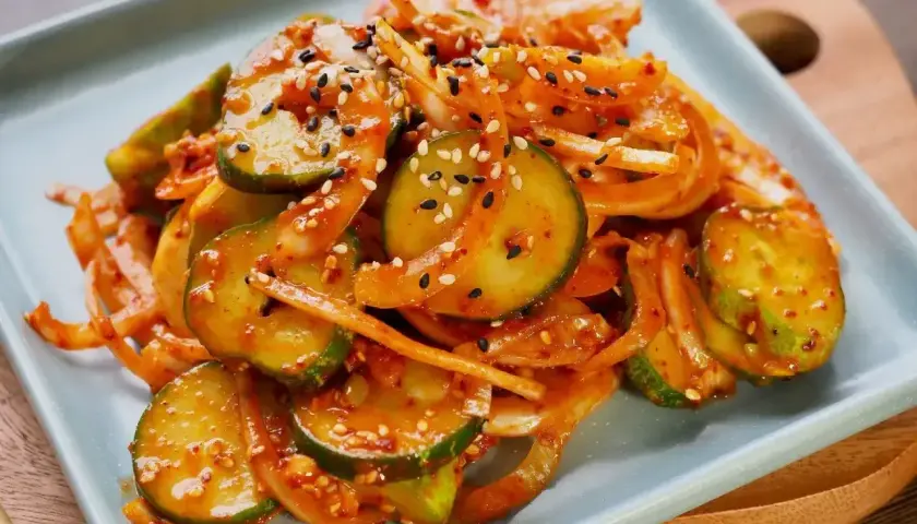Pikantne ogórki po koreańsku z cebulą i sezamem, podane na jasnoszarym talerzu.