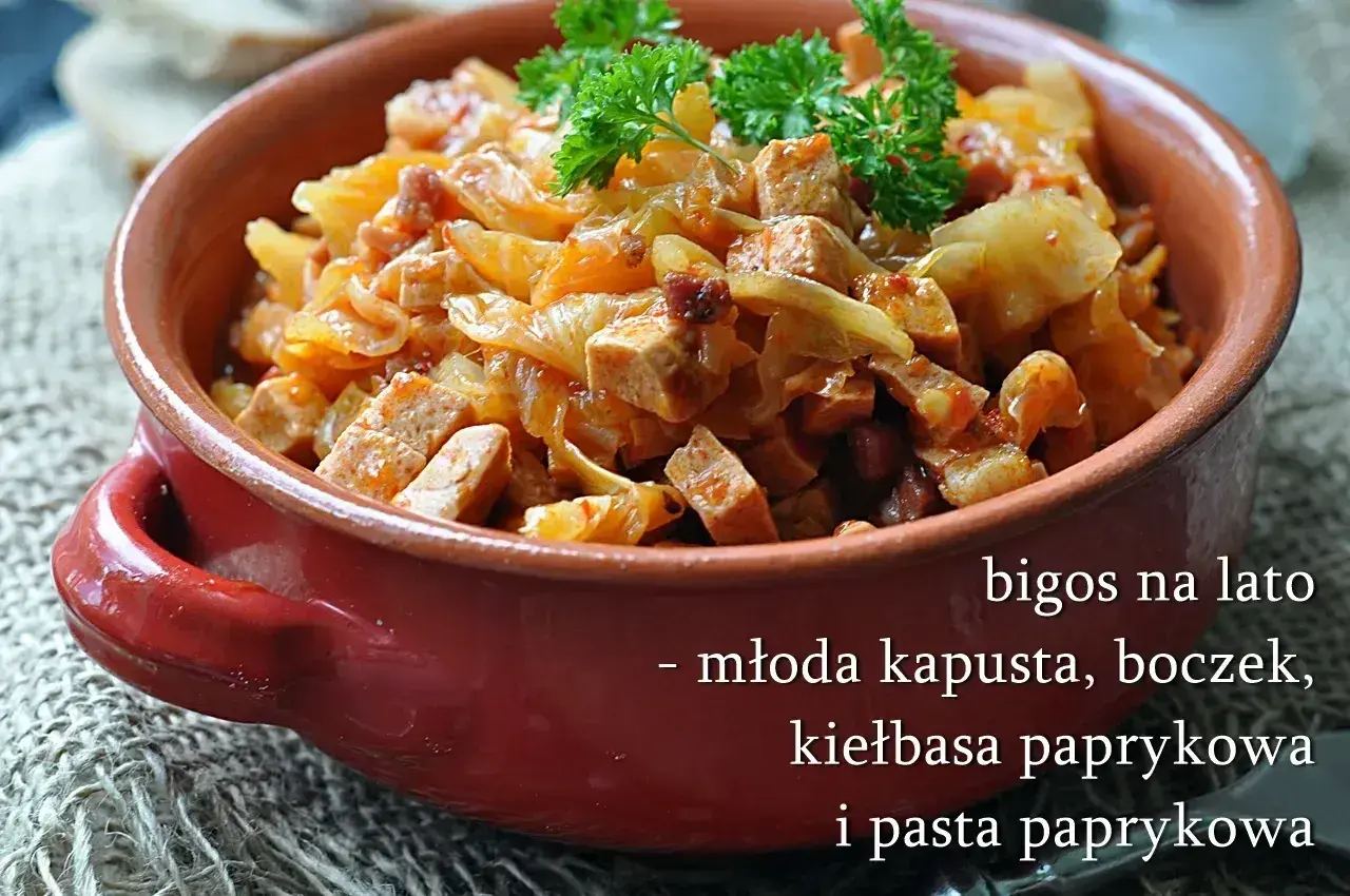 Pyszny bigos z młodej kapusty z boczkiem i kiełbasą paprykową, podany w glinianym naczyniu, udekorowany natką pietruszki.