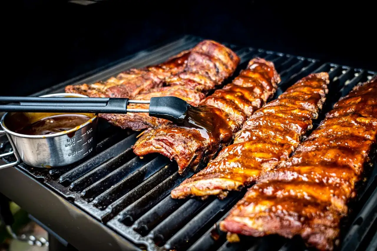 Soczyste żeberka z grilla pokryte błyszczącym sosem BBQ, pędzel właśnie nakłada kolejną porcję.