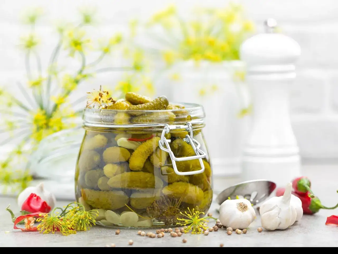 Słoik pełen chrupiących ogórków po kartusku, otoczony czosnkiem, chili i koprem. Idealne na letnie przetwory.