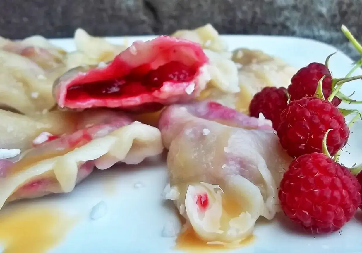 Pyszne pierogi z malinami, polane syropem, z dodatkiem świeżych malin.