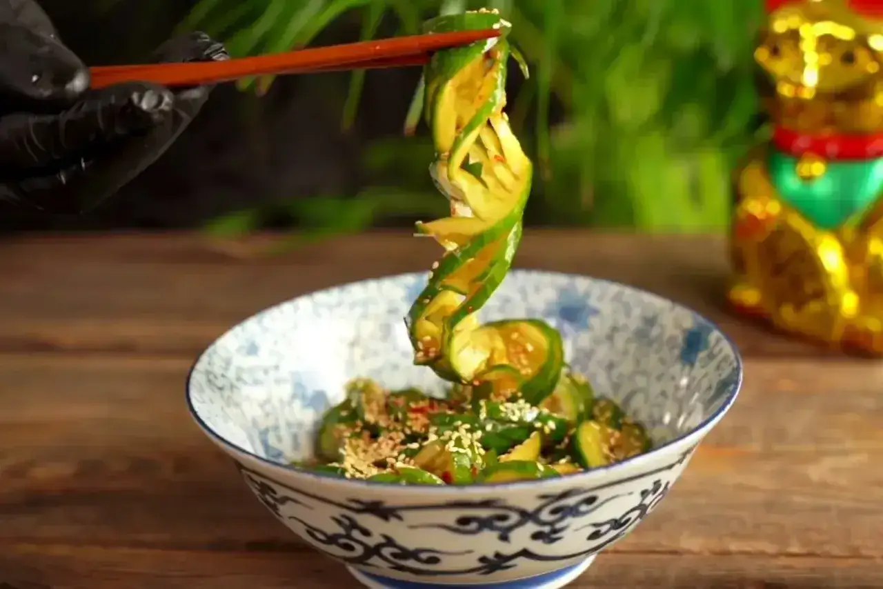 Chopsticks podnoszą spiralnie pokrojonego ogórka z miski. To pyszna tajska sałatka z ogórka, posypana sezamem.